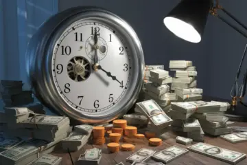 Clock face with gears and money on a table under a lamp light.