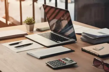Office desk with laptop showing graph, business documents, fountain pen, potted plant, and calculator.